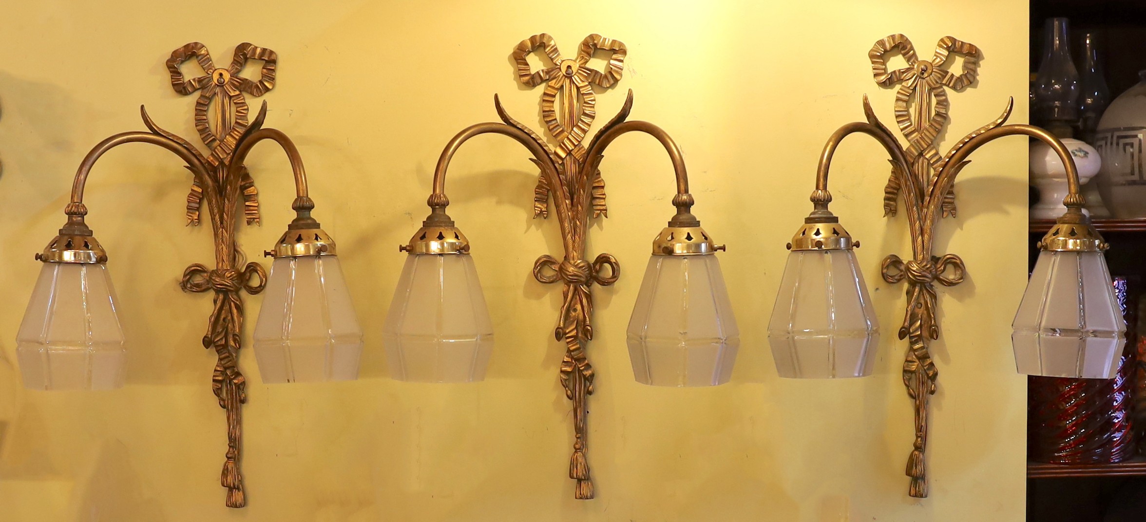 A set of three early 20th century English gilt metal twin branch wall lights with frosted glass shades, height 51cm. width 36cm